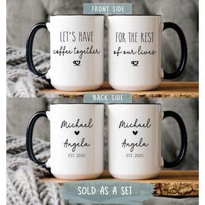 May include: Two white ceramic mugs with black handles. One mug says "Let's have coffee together" and the other says "For the rest of our lives". The back of the mugs have the names "Michael" and "Angela" with a heart and the year "EST. 2025".