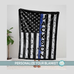 May include: A black and white American flag with a thin blue line down the center. The name "JACKSON" is written vertically in white letters on the blue line. The flag is on a soft, plush blanket.