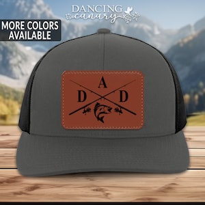 May include: A gray and black trucker hat with a brown leather patch that says "DAD" with a fishing rod and fish design.