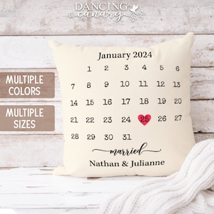 May include: A white pillow with a calendar design for January 2024. The 25th is highlighted with a red heart and the text "married" is written below the calendar with the names Nathan & Julianne.