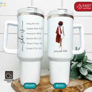 May include: White tumbler with a handle, featuring the text "she is" and inspirational phrases. The back of the tumbler has a graduation illustration with the name "Sarah 2026". The tumbler is dishwasher safe.