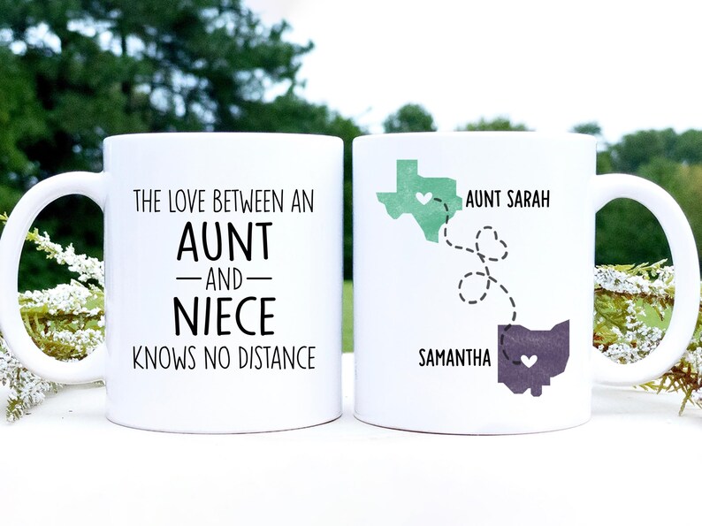 May include: Two white coffee mugs with black text. The mug on the left says "The love between an aunt and niece knows no distance". The mug on the right has a map of Texas and Ohio with the names "Aunt Sarah" and "Samantha" and a heart in each state.