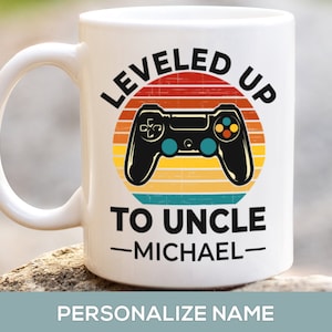 May include: White ceramic coffee mug with a retro-style design featuring a video game controller and the text "LEVELED UP TO UNCLE -MICHAEL-"