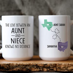 May include: Two white ceramic mugs with black text and a heart design. One mug says "The love between an aunt and niece knows no distance". The other mug has a map of Texas and Ohio with the names "Aunt Sarah" and "Samantha" and a heart design.