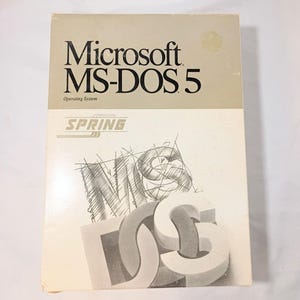 Op de afbeelding: Een rechthoekige softwaredoos voor het Microsoft MS-DOS 5 besturingssysteem. De doos is beige en wit met zwarte tekst die Microsoft MS-DOS 5 en Operating System leest. Het bevat een afbeelding met het woord MS-DOS in gestileerde letters.