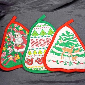 May include: Three Christmas-themed pot holders with red trim. One features Santa Claus, another has the word "NOEL", and the third displays a deer and a Christmas tree. Each has a loop for hanging.
