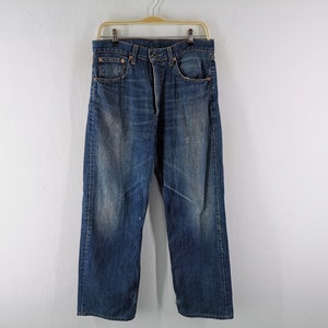 May include: Blue denim jeans with a faded wash and a straight leg fit. The jeans are hanging on a wooden hanger against a white background. The jeans have a classic five-pocket design.