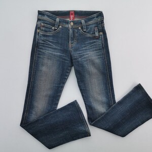 Pu&ograve; includere: Jeans in denim blu scuro con lavaggio sbiadito, caratterizzati da un classico design a cinque tasche, chiusura con bottone e zip e una leggera svasatura sul fondo delle gambe. La vita presenta passanti per cintura e un'etichetta rossa interna.