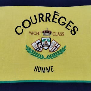 Op de afbeelding: Gele stof met het woord "COURR&Egrave;GES" in zwart, bovenaan gebogen. Daaronder staat "YACHT CLASS" in goud. Een wapen met een kroon en schilden is gecentreerd, met "SPORT" in het midden. Het woord "HOMME" staat onderaan.