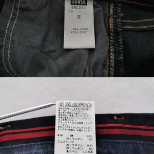 K&ouml;nnte beinhalten: Nahaufnahme der Innenseite einer dunkelblauen Jeans. Die Jeans hat einen rot-schwarz gestreiften Bund und ein wei&szlig;es Etikett mit der Marke "EDWIN" und der Gr&ouml;&szlig;e "S". Das Etikett enth&auml;lt auch Produktcodes und Waschanweisungen.