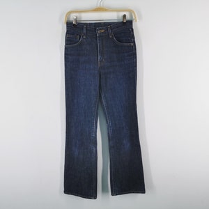 May include: Dark wash denim jeans with a high waist and flared leg, hanging on a wooden hanger. The jeans have classic five-pocket styling and a button and zipper closure. The fabric appears to be a medium weight.
