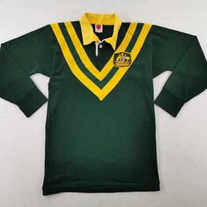 May include: Green long-sleeve rugby shirt with yellow stripes and collar. Features an emblem on the chest. The shirt has a button-down collar and ribbed cuffs. The shirt is approximately 28 inches long.