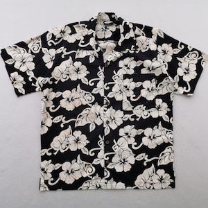 May include: Black button-down shirt with a white floral pattern. The short-sleeved shirt features a classic collar and a single chest pocket. The floral design includes hibiscus flowers and leaves.