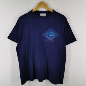 May include: Navy blue t-shirt with a diamond-shaped graphic on the chest. The graphic features a blue and silver design with the letters "C.I.T.T." below. The shirt is hanging on a wooden hanger against a white background.