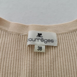 May include: Close-up of a beige ribbed knit top with a round neckline. A label with the brand name "courr&egrave;ges" and the size "38" is visible. The fabric has vertical ribbing.