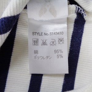 May include: A white and navy blue striped ribbed fabric with a white care label attached. The label displays STYLE No. 6143410, laundry care symbols, and the material composition of 95% cotton and 5% polyurethane in Japanese text characters.