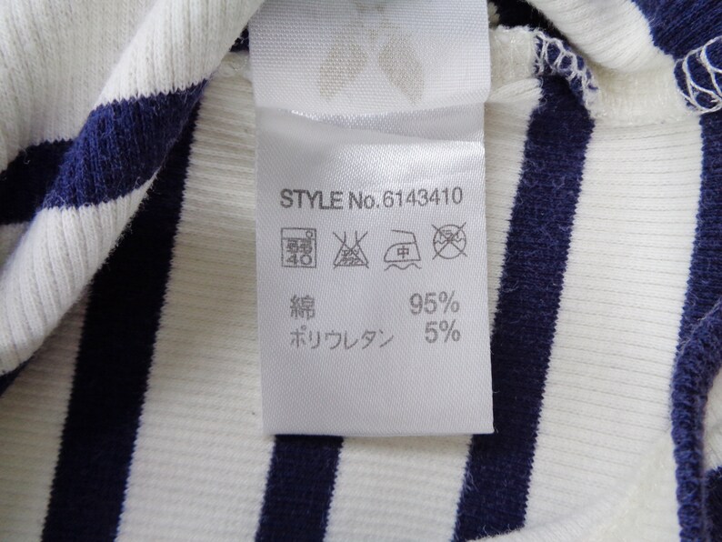 May include: A white and navy blue striped ribbed fabric with a white care label attached. The label displays STYLE No. 6143410, laundry care symbols, and the material composition of 95% cotton and 5% polyurethane in Japanese text characters.