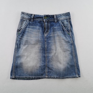 Pu&ograve; includere: Una gonna di jeans blu con un lavaggio sbiadito. La gonna ha un classico design a cinque tasche, una chiusura con bottone e cerniera e cuciture verdi sulle tasche. La gonna &egrave; lunga circa 46 cm.