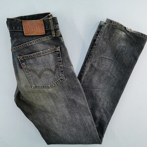 May include: Faded black denim jeans with a classic five-pocket design. Features a leather patch with the brand name "EDWIN" and a red logo on the back pocket. The jeans are folded and laid flat.