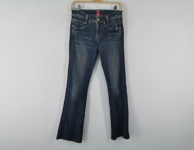 Pu&ograve; includere: Jeans in denim blu scuro con lavaggio sbiadito, design classico a cinque tasche, chiusura con bottone e cerniera e taglio a gamba dritta. I pantaloni presentano cuciture color rame e una piccola etichetta rossa sulla tasca anteriore.