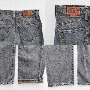 May include: Faded blue denim jeans with a classic five-pocket design. The jeans feature a leather patch with the brand name "EDWIN" and a red tab detail. The denim has a worn look, with visible stitching and a straight leg cut.