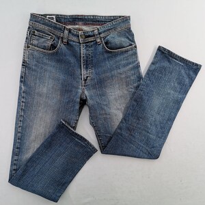 May include: Blue denim jeans with a classic five-pocket design. The jeans have a button and zip closure, belt loops, and a faded wash. The legs are straight cut. The jeans are laid flat on a white surface.