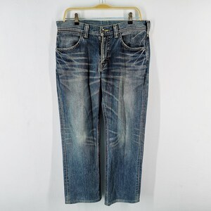 May include: Blue denim jeans hanging on a gold hanger. The jeans have a classic five-pocket design and a straight leg cut. The denim has a faded, worn look with lighter areas and subtle distressing.