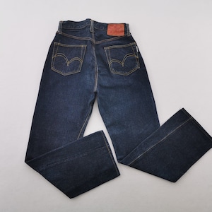 May include: Dark blue denim jeans with yellow stitching and two back pockets. The jeans have a classic five-pocket design, a leather patch, and a straight leg. The jeans are laid flat on a white surface.