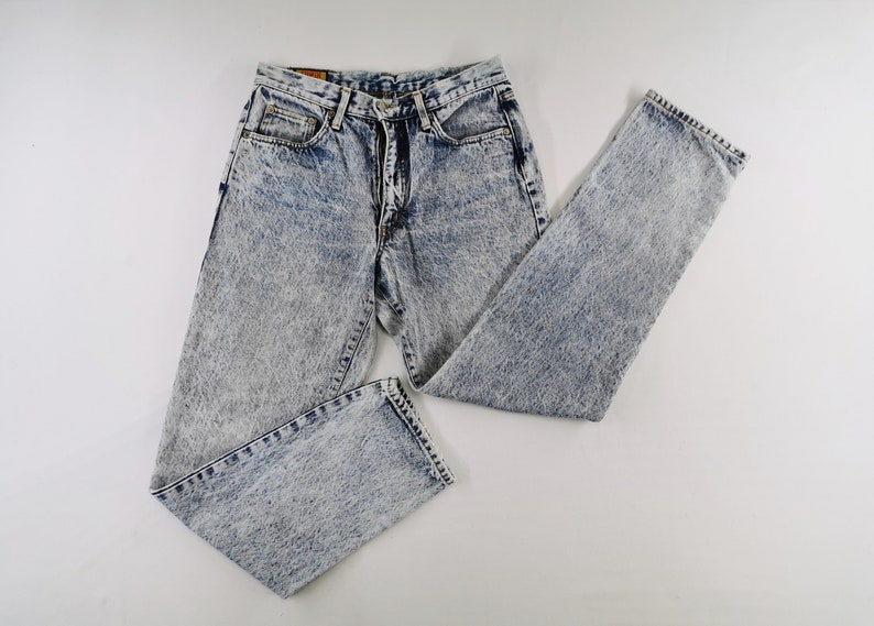 K&ouml;nnte beinhalten: Jeans aus Acid-Wash-Denim mit einem hellblauen und wei&szlig;en Muster. Die Jeans haben ein klassisches F&uuml;nf-Taschen-Design und ein gerades Bein. Die Jeans liegen flach auf einer wei&szlig;en Oberfl&auml;che.
