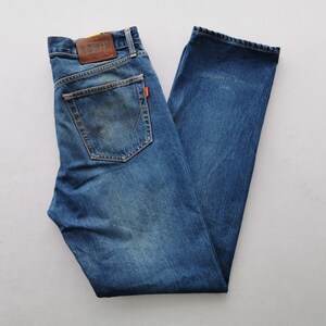 Puede incluir: Vaqueros de mezclilla azules con un dise&ntilde;o cl&aacute;sico de cinco bolsillos. Cuenta con un parche de cuero marr&oacute;n en la cintura trasera y una peque&ntilde;a etiqueta naranja. Los vaqueros est&aacute;n planos, mostrando el lavado descolorido y los detalles de costura.
