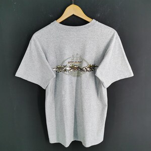 May include: A heather gray t-shirt with a crew neck and short sleeves. The back of the shirt features a circular design with the words "BODY GLOVE" and a floral pattern in shades of brown, green, and white.