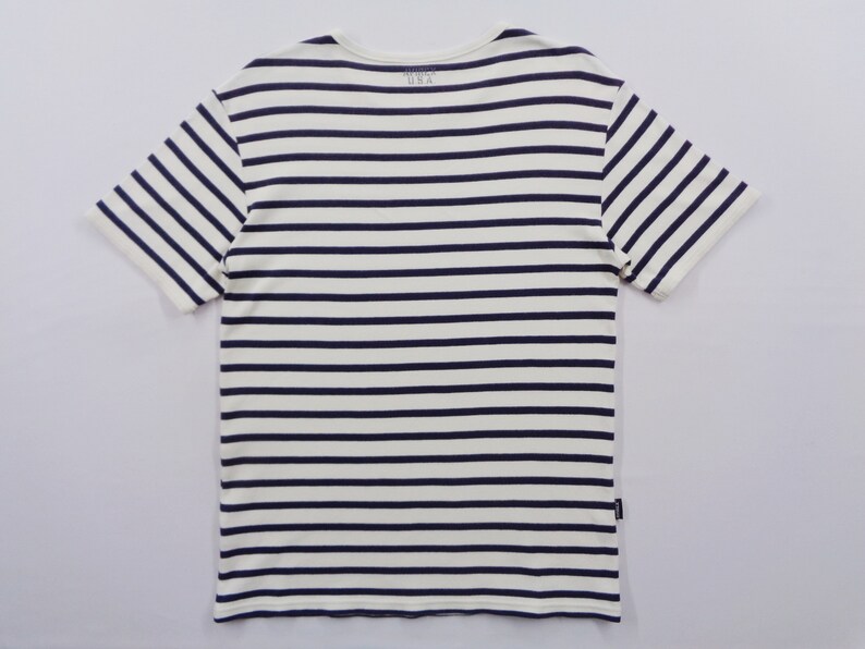 May include: A short-sleeve t-shirt featuring a horizontal striped pattern in navy blue and off-white. The garment has a crew neckline and includes the text "MADE IN USA" printed on the inside collar area, along with a small black tag on the side seam.