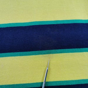 Op de afbeelding: Close-up van een gele stof met horizontale strepen in marineblauw en groen. De stof lijkt een gebreid materiaal te zijn, mogelijk katoen of een mix. De strepen zijn gelijkmatig verdeeld en cre&euml;ren een gedurfd, grafisch patroon.