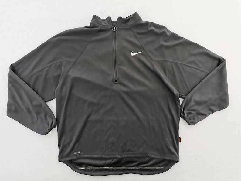 Pu&ograve; includere: Top sportivo grigio antracite con zip a un quarto e logo Nike bianco. Il top a maniche lunghe ha un collo alto ed &egrave; realizzato in materiale leggero e traspirante. La scritta "DRI-FIT" &egrave; stampata in basso a sinistra.