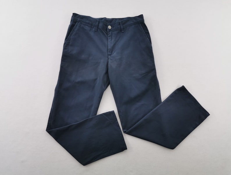 May include: Navy blue pants with a button closure and pockets. The pants are made of a solid, durable fabric and have a classic, straight-leg design. The pants are laid flat on a white surface.