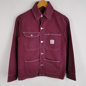 May include: A burgundy and black striped jacket with a collared neckline and button-up closure. The jacket features four front pockets, white stitching, and a small patch on the chest. The jacket is hanging on a wooden hanger.