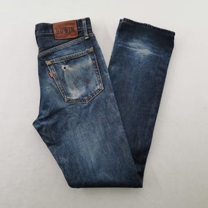 K&ouml;nnte beinhalten: Dunkelblaue Jeans mit verwaschenem Effekt und Used-Details. Die Jeans haben ein klassisches F&uuml;nf-Taschen-Design, einen Lederaufn&auml;her mit Markenname und ein rotes Logo-Etikett. Die Jeans liegen flach auf einer wei&szlig;en Oberfl&auml;che.