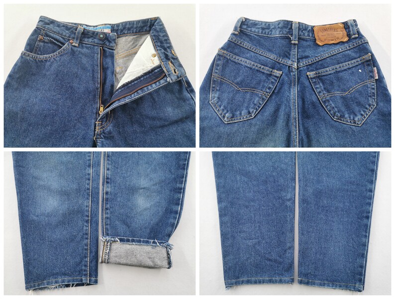 May include: Blue denim jeans with a classic five-pocket design. The jeans feature a zip fly, button closure, and a leather patch on the back. The cuffs are rolled up, revealing the interior fabric. The jeans are a medium wash.