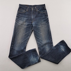May include: Dark wash denim jeans with a classic five-pocket design. The jeans have a faded appearance with subtle wear marks, and a button and zipper closure. The jeans are laid flat on a white surface.