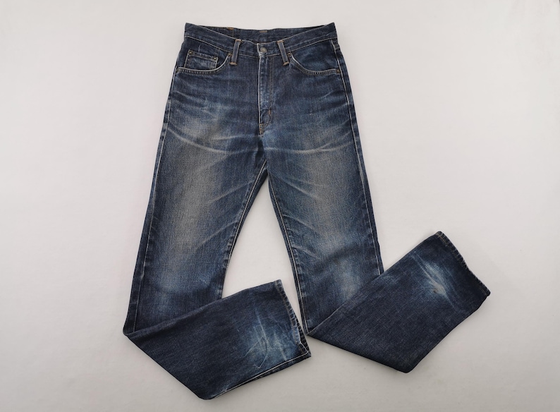K&ouml;nnte beinhalten: Dunkelblaue Jeans mit klassischem F&uuml;nf-Taschen-Design. Die Jeans haben ein verwaschenes Aussehen mit dezenten Gebrauchsspuren und einen Knopf- und Rei&szlig;verschluss. Die Jeans liegen flach auf einer wei&szlig;en Oberfl&auml;che.