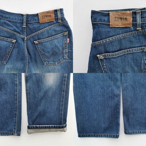 May include: Blue denim jeans with a classic five-pocket design. Features a brown leather patch with "EDWIN" branding on the back waistband. The jeans have a straight leg cut and a red tag on the back pocket.