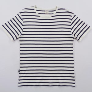 May include: A short-sleeved crew neck t-shirt featuring a horizontal striped pattern in dark navy blue and off-white. The garment has a ribbed neckline and a small rectangular brand label attached to the lower left side seam near the hem.