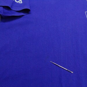 May include: A royal blue t-shirt with a white and red graphic design on the front. The sleeve has the word "FILA" printed in white. The shirt is made of a soft material.