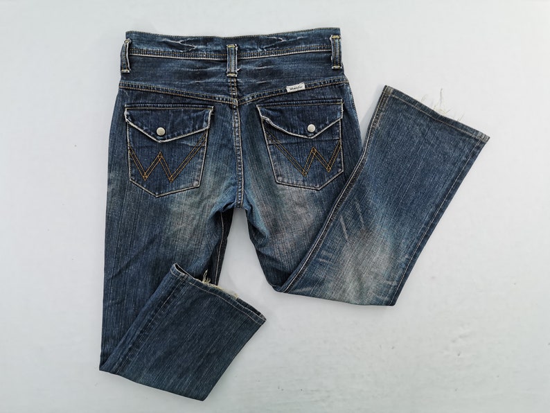 Puede incluir: Vaqueros de mezclilla azul con un lavado descolorido. Incluye dos bolsillos traseros con un dise&ntilde;o de costura caracter&iacute;stico, dos bolsillos delanteros y una etiqueta de la marca Wrangler. Los vaqueros tienen un dise&ntilde;o cl&aacute;sico de cinco bolsillos.