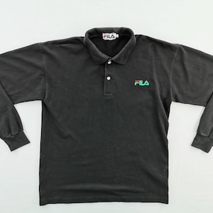 May include: Black long-sleeve polo shirt with a collar and button closure. The shirt features the Fila logo in green and red on the chest and the Fila logo on the collar.