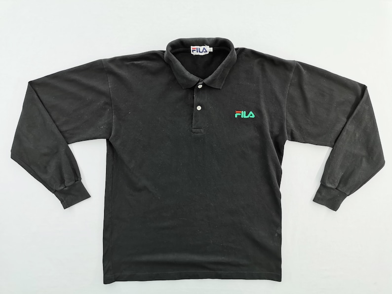 May include: Black long-sleeve polo shirt with a collar and button closure. The shirt features the Fila logo in green and red on the chest and the Fila logo on the collar.