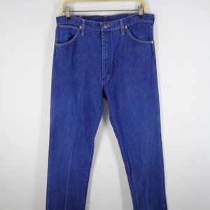 May include: Classic blue denim jeans hanging on a wooden hanger. The jeans have a button and zipper closure, front and back pockets, and a straight leg design. The denim is a solid, medium blue color.
