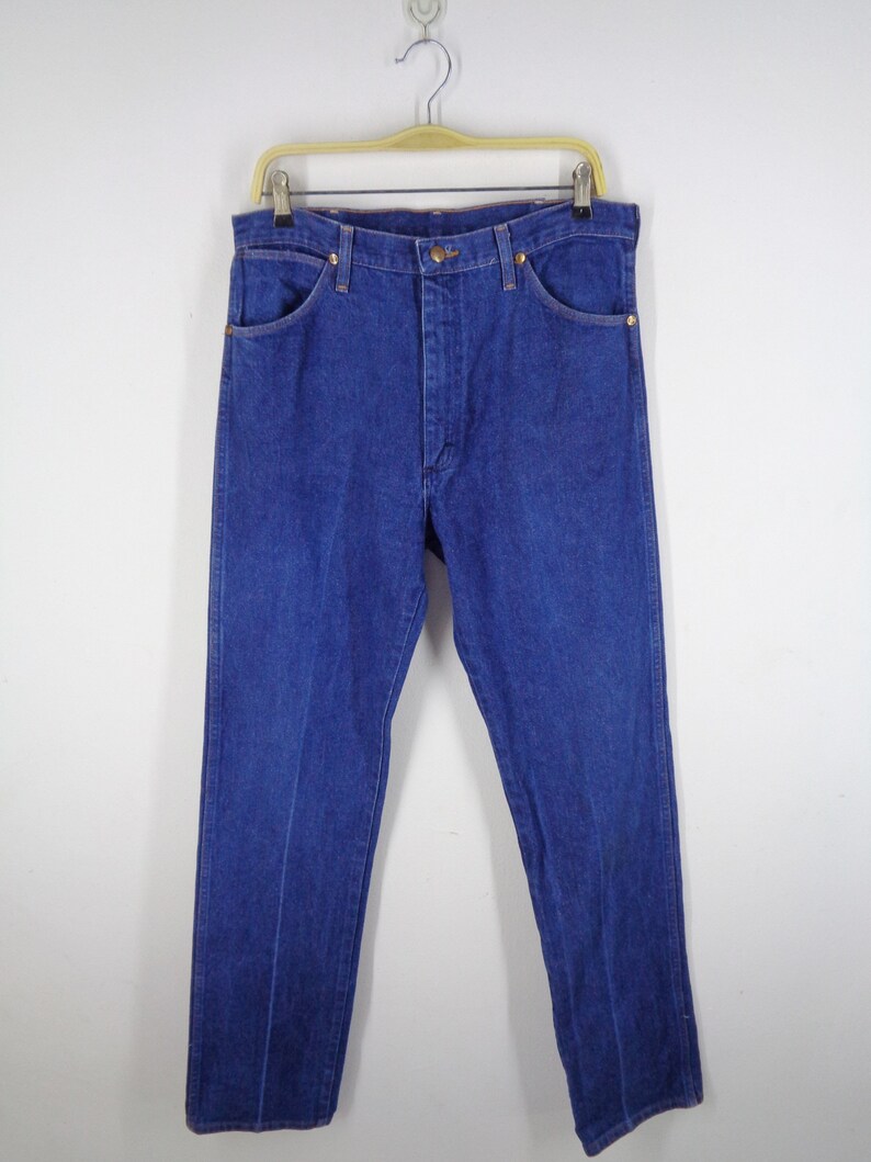 May include: Classic blue denim jeans hanging on a wooden hanger. The jeans have a button and zipper closure, front and back pockets, and a straight leg design. The denim is a solid, medium blue color.