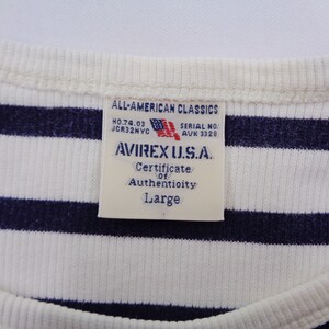 May include: A white and navy blue striped ribbed shirt featuring a rectangular tag at the neckline. The tag reads ALL-AMERICAN CLASSICS, NO.74.03, JCR32NYC, SERIAL NO. AVK 3328, AVIREX U.S.A., Certificate of Authenticity, and the size Large.