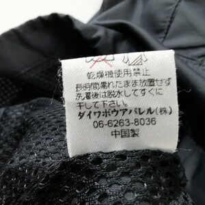 May include: Close-up of a black garment with a white tag. The tag has Japanese text and symbols, including a no-dry-clean symbol. The garment has a mesh lining.
